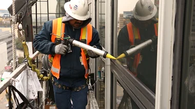 A worker opts to reseal the glazing of an exterior window instead of replacing the entire fixture, a more economical choice.