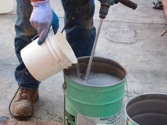 A worker using an open drum mixer to properly mix Tremco coating prior to application.