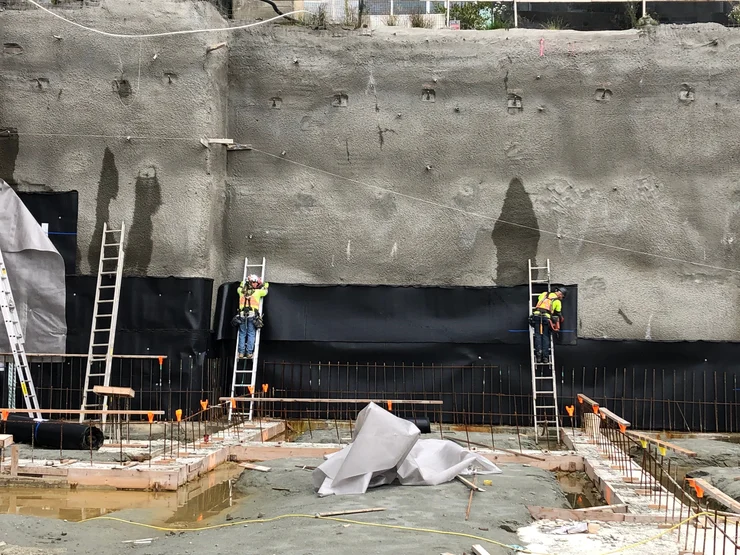 Applying blindside waterproofing in the initial phases at an excavated construction site.