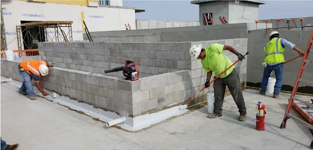 Waterproof block trails are installed on a rooftop planter assembly by a team of workers.