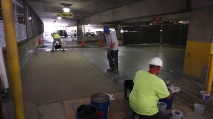 A group of workers are shown applying PUMA waterproofing technology to the exposed concrete surface inside a parking structure.