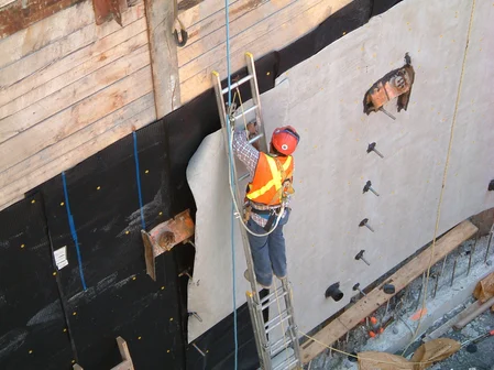 A worker shown installing high strength plastic sheet waterproofing membrane to a wooden building surface.