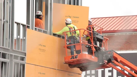 A team of workers installing preassembled Tremco insulated paneling on a new structure.