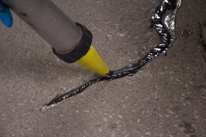 Tremco Dymonic 100 polyurethane sealant is shown being applied into a concrete crack.