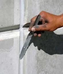 A worker tooling the sealant bond line with a spatula to ensure proper adhesion.