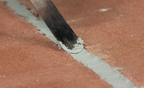 A spatula is shown smoothing a sealant bead after being applied to a substrate.