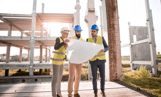 An architect, inspector, and site supervisor shown examining pre-construction plans for a new building structure to verify that the design complies with all regulatory standards.