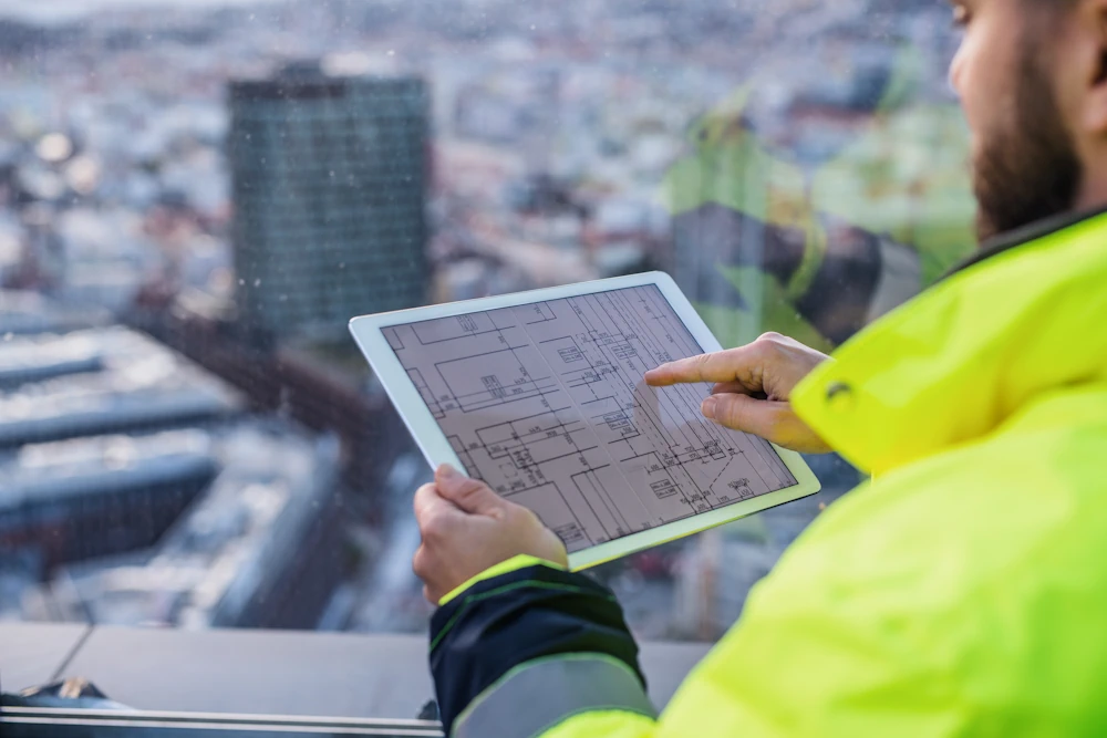 The picture depicts a person using a tablet to look at building blueprints. 