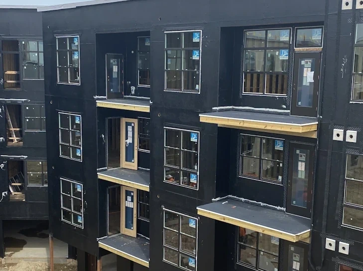 A several story building under construction with black waterproofing on the outside.